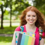 Smiling student holding notebooks on college campus