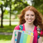 Smiling student holding notebooks on college campus